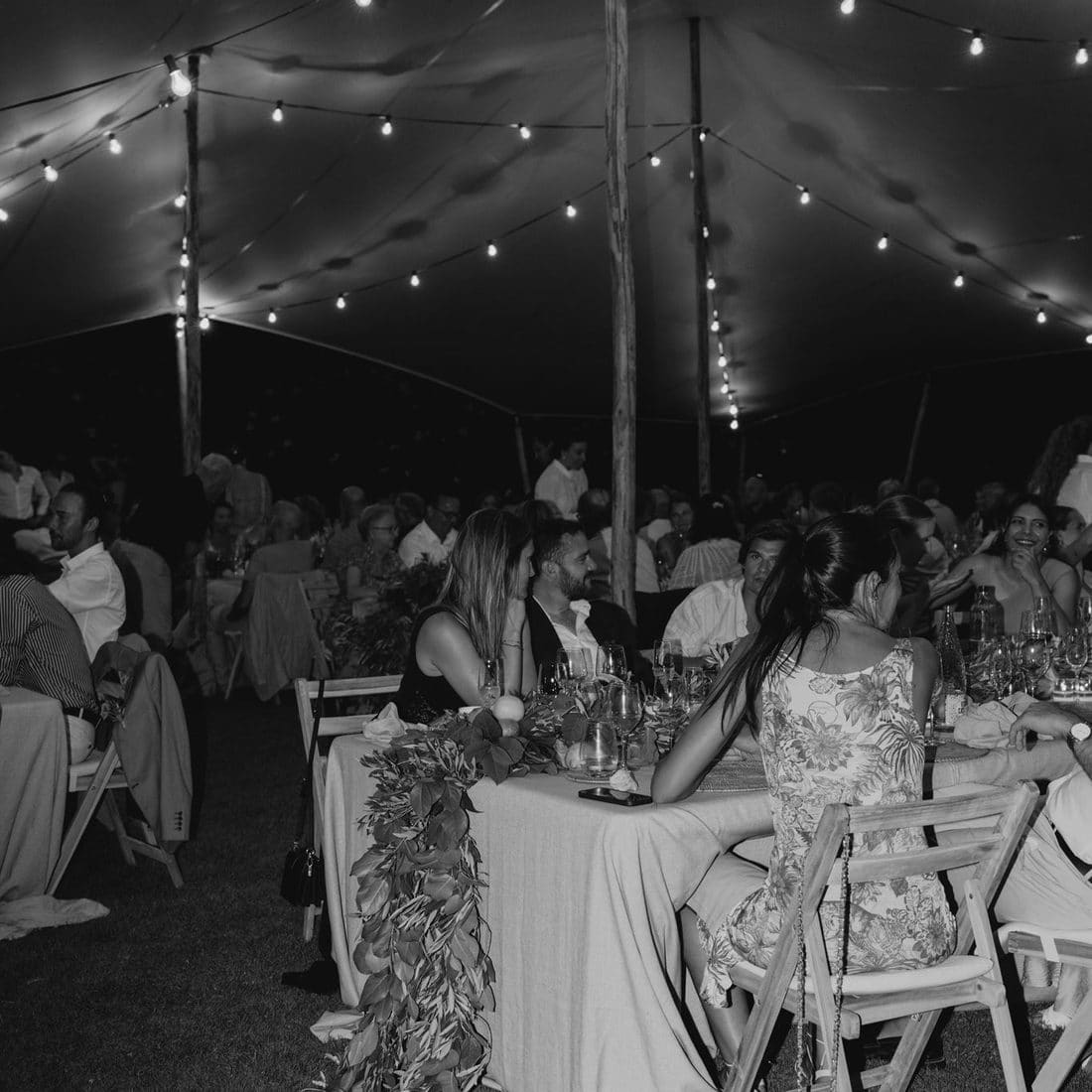 Convidats sopant sota una carpa il·luminada amb garlandes de llums en un banquet de casament