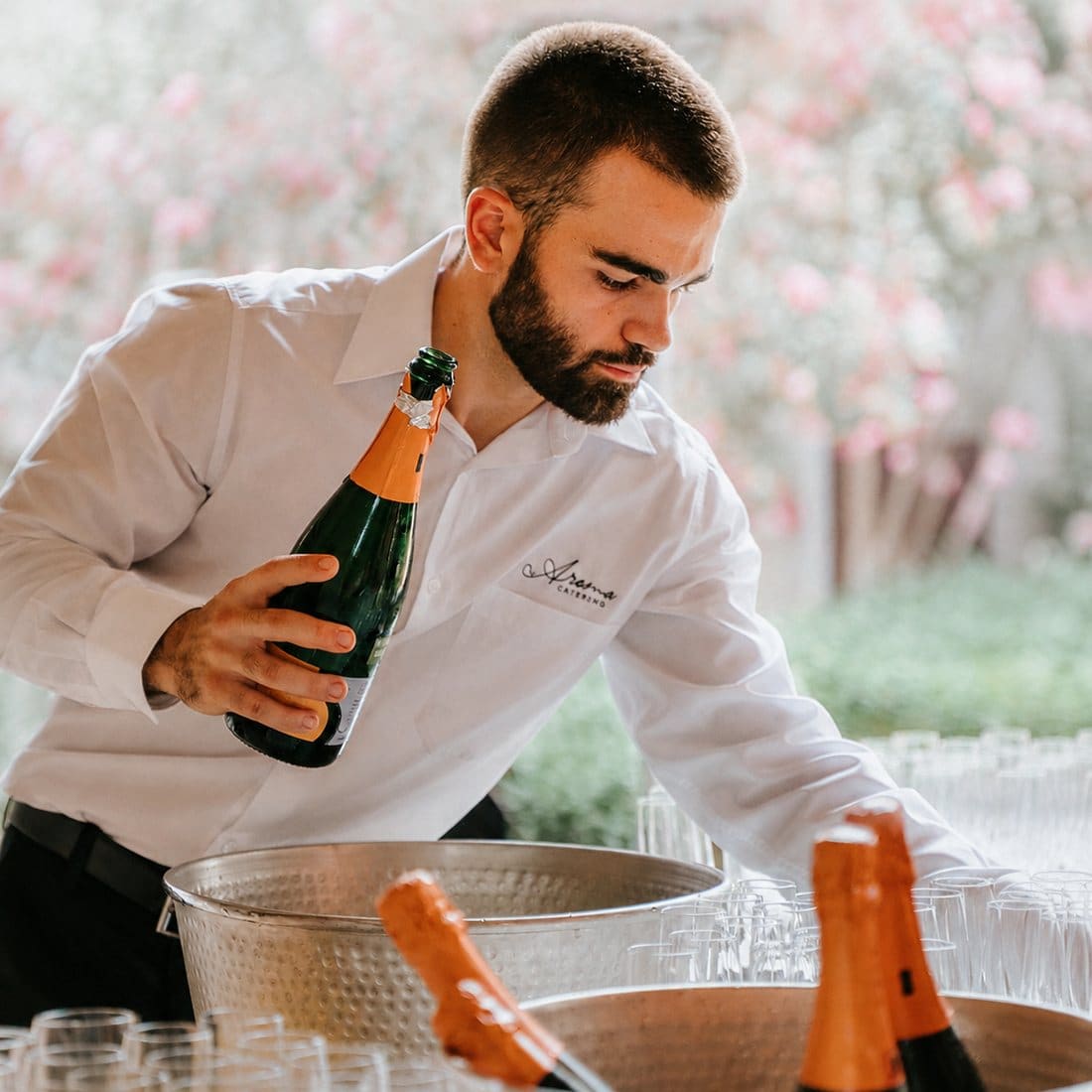Cambrer d’Aroma Catering amb una ampolla de cava al costat de les galledes de gel i les copes