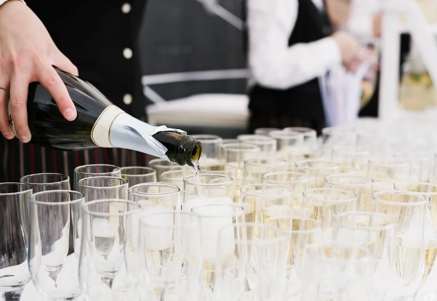 Camarero llenando filas de copas de cava con una botella