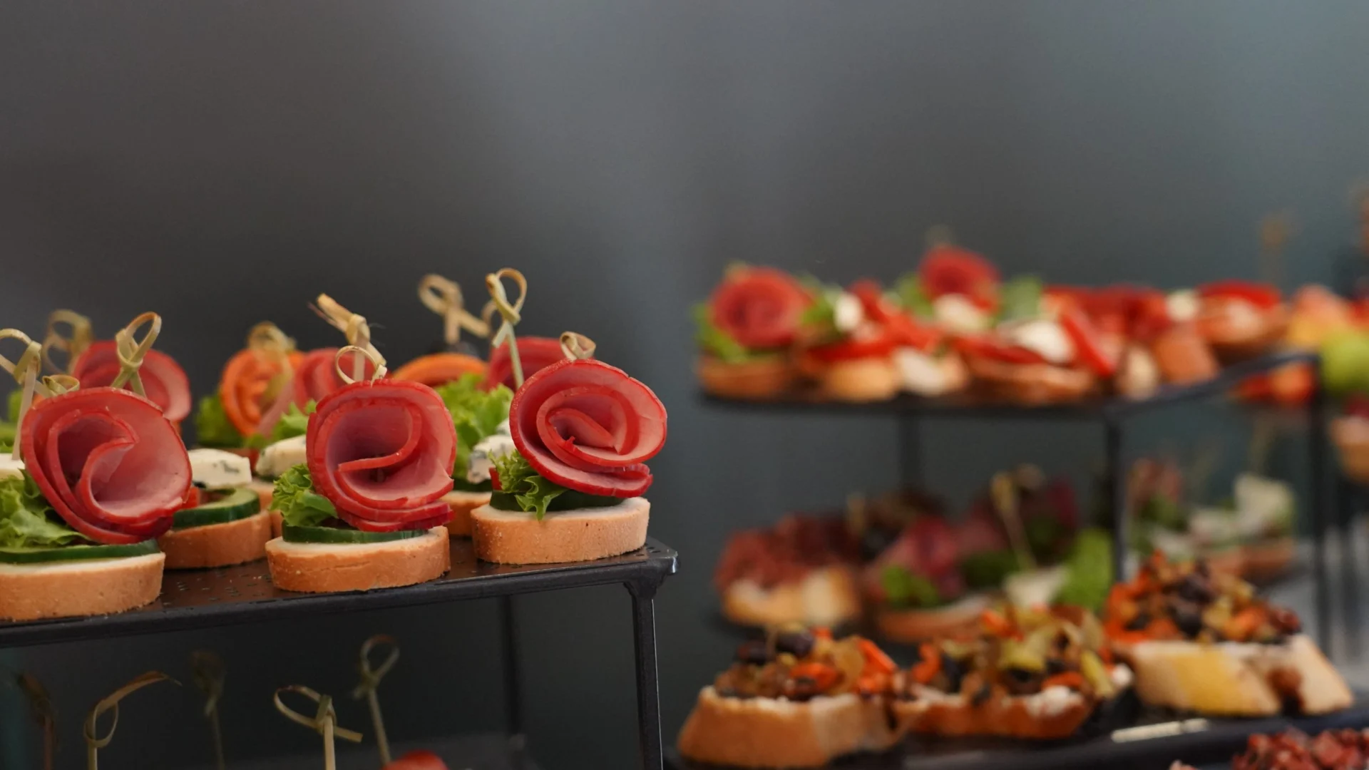 Canapés en expositores negros con embutido enrollado, tomate y lechuga