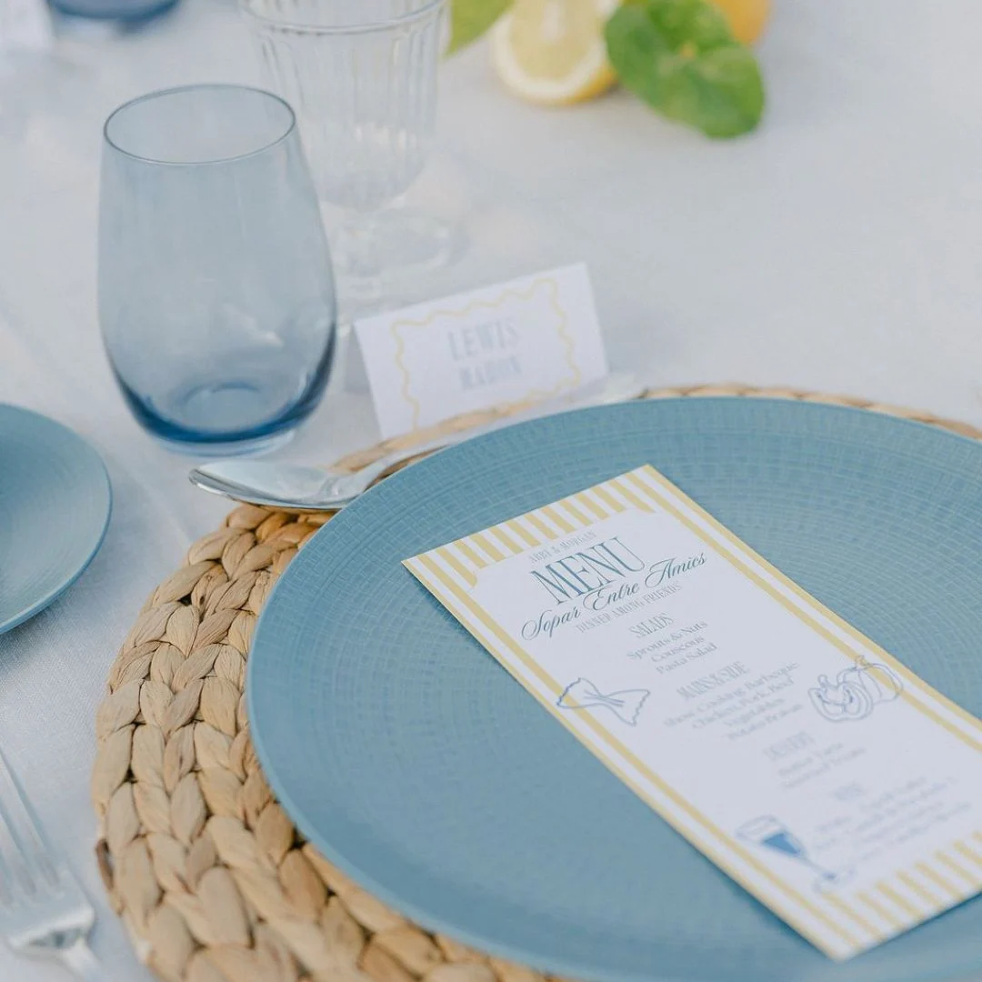Place setting with blue plate on woven mat, blue glass and menu card