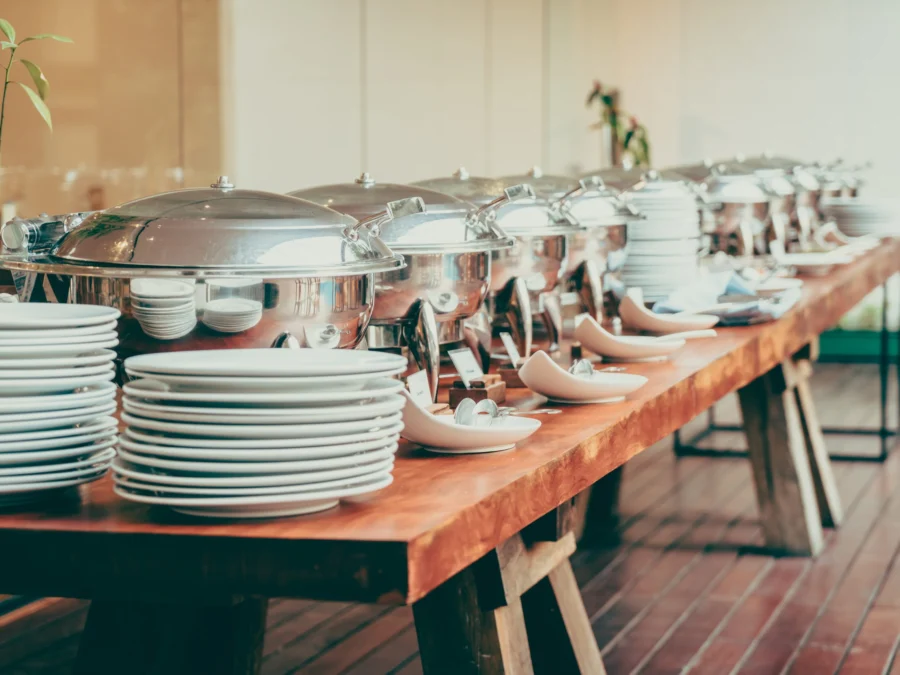 Buffet table with stainless chafing dishes and stacks of white plates