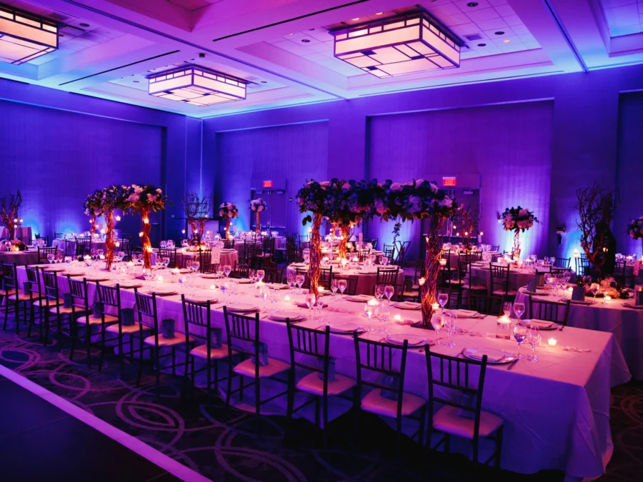 Sala de banquets amb llum violeta, taula llarga i centres florals alts
