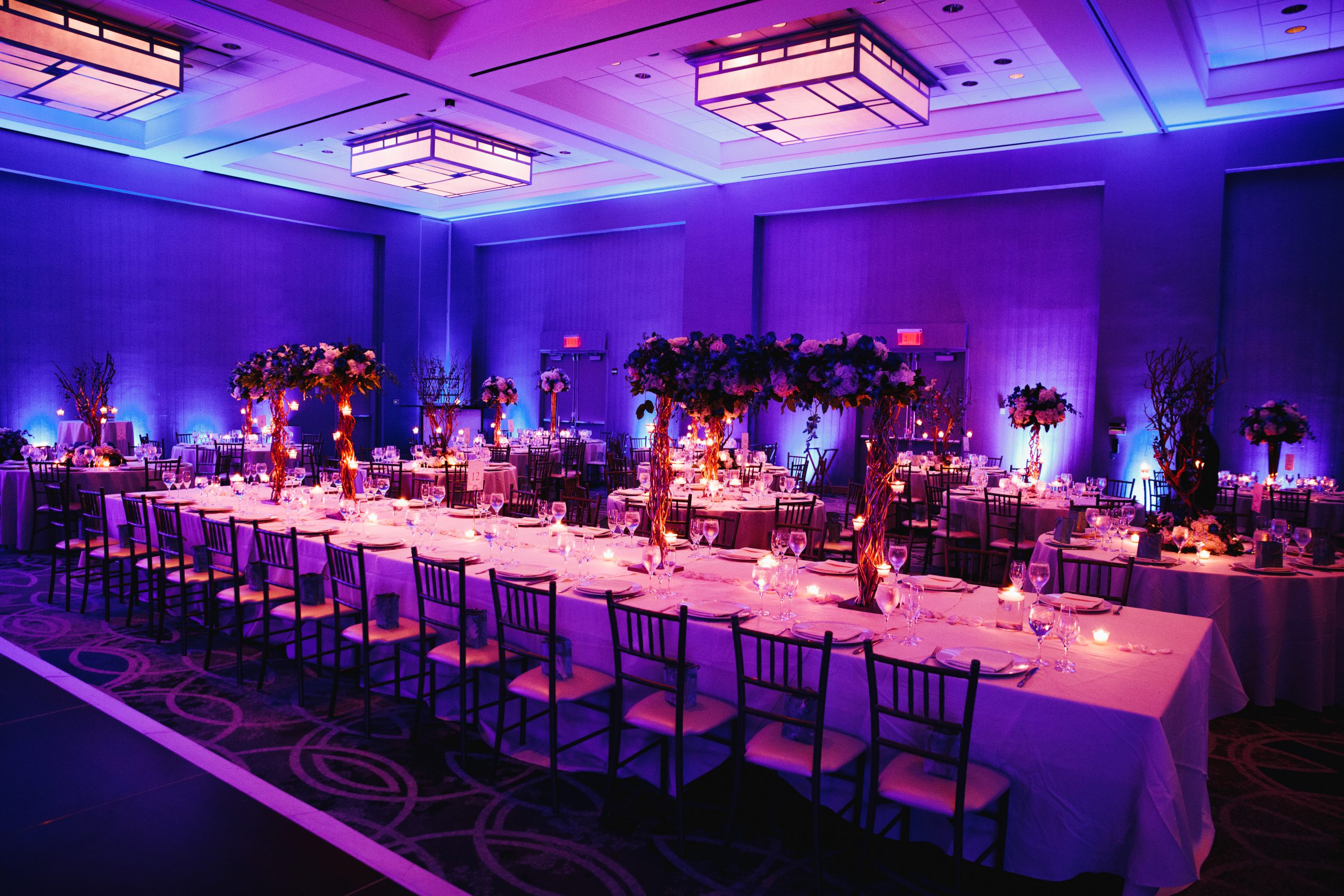 Salón de banquetes con luz violeta, mesa larga y centros florales altos