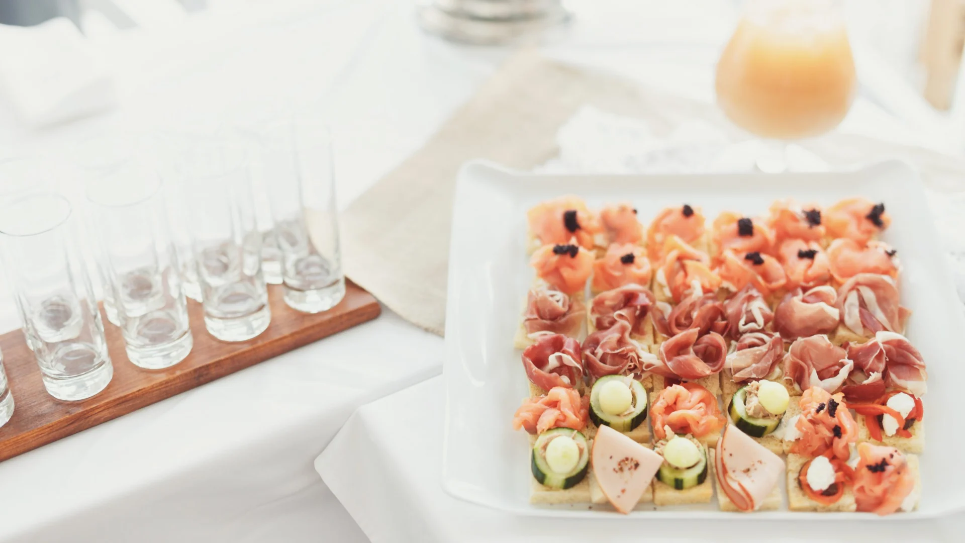 Square platter of smoked salmon, ham and cucumber canapés with shot glasses