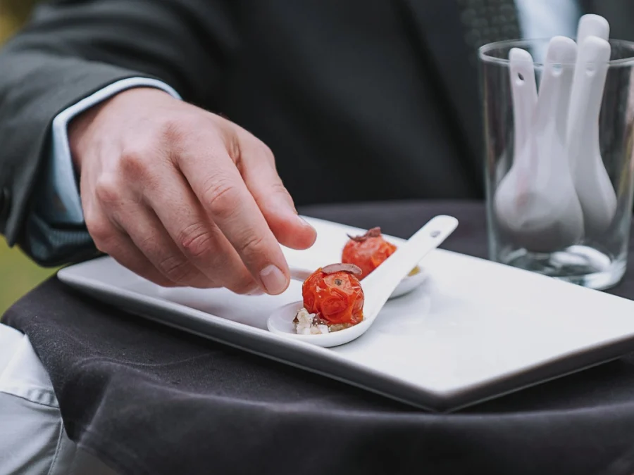 Camarero de traje sirviendo cucharillas con tomate confitado en bandeja blanca