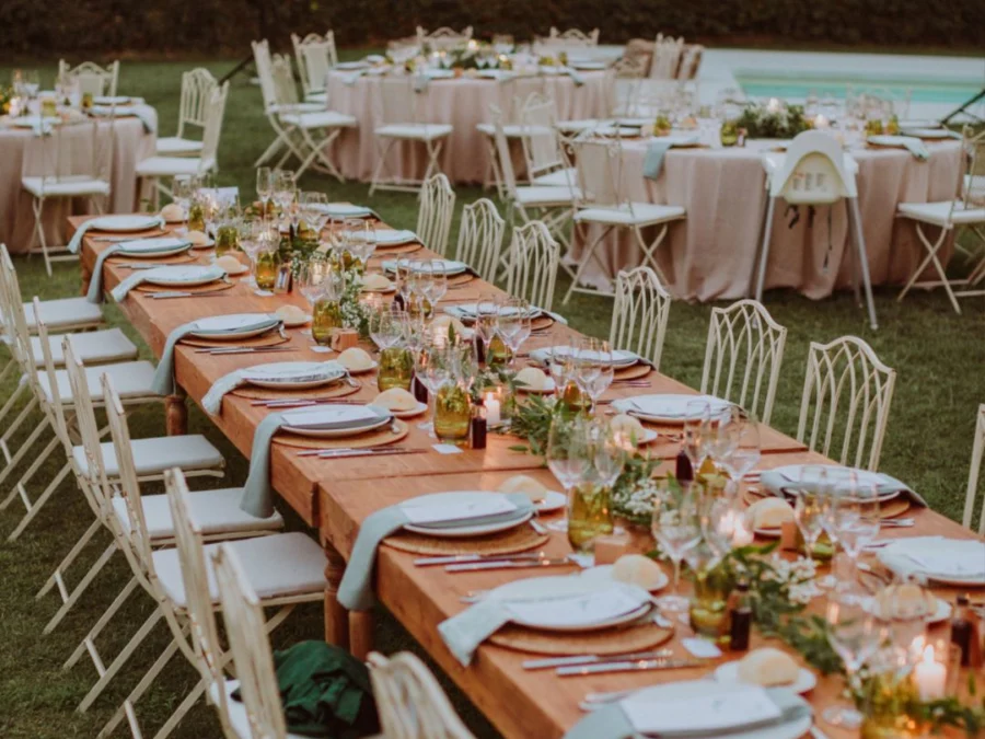Long wooden table on the lawn with candles beside a swimming pool