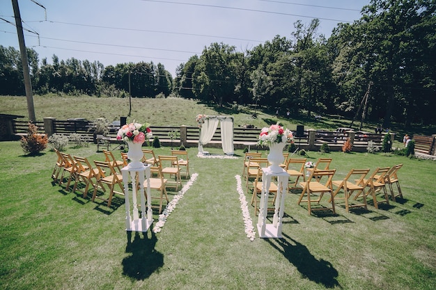 Outdoor ceremony on grass with wooden chairs, fabric arch and pink flowers