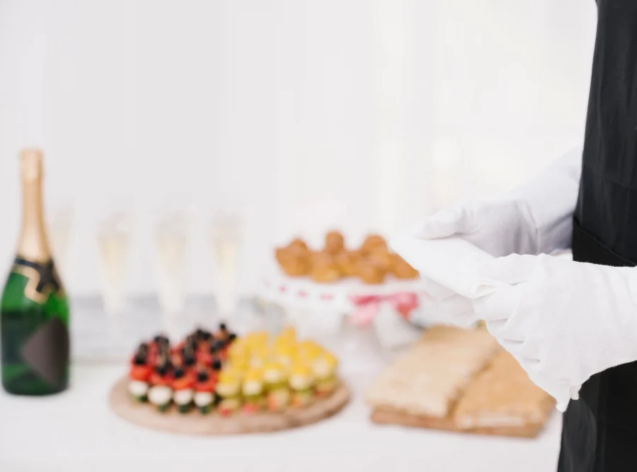 Waiter in black apron and white gloves beside a table of canapés