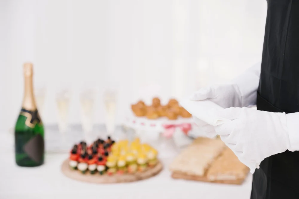 Waiter in black apron and white gloves beside a table of canapés