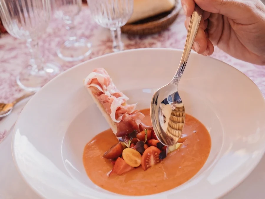 Bowl of chilled tomato soup with cherry tomatoes and a ham roll