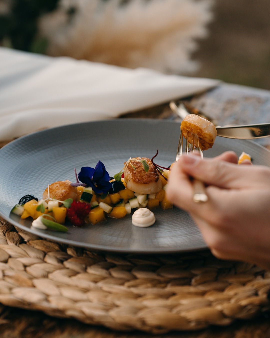 Mà amb forquilla agafant una vieira daurada d'un plat amb daus de mango